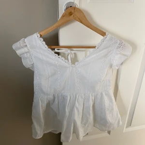 Vit blus med spetsdetaljer från SHEIN - Söt vit blus från SHEIN med v-ringning, spetsdetaljer och volang vid axlarna. Blusen har korta ärmar, knytning i ryggen och dekorativa knappar. Perfekt för vår och sommar!