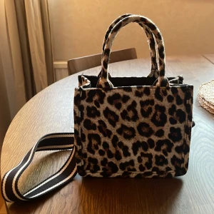 Leopardmönstrad handväska från H&M - Säljer en handväska från H&M med leopardmönster. Väskan har två handtag och en bred, avtagbar axelrem i svartvitt. Perfekt storlek för det viktigaste och ger en cool touch till din outfit.