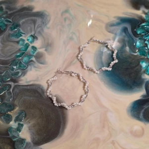 Silvriga örhängen med pärldetaljer - Säljer ett par snygga silvriga örhängen i större ringmodell med oregelbunden form och små vita pärlor längs hela ringen. Perfekta för att ge din look lite extra glans och stil.