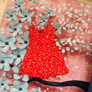 Somrig blommig klänning – storlek XS - Lätt och mjuk klänning med blommönster i härlig röd färg. Djup V-ringning, smala axelband och ingen dragkedja eller resår bak – passar bäst för storlek XS. Superfin passform, perfekt för sommardagar eller fest. Endast använd en gång – i nyskick. 