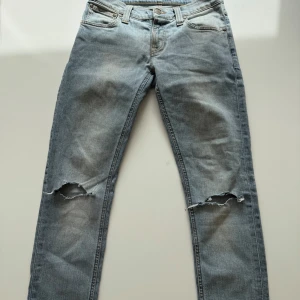 Ljusblå slitna jeans från Nudie  - Ljusblå jeans från Nudie Jeans med raka ben och slitningar över knäna. Klassisk femficksmodell med knappgylf och tydliga slitdetaljer framtill. Perfekta för en avslappnad och trendig look.