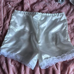 Vita satinskjorts med spetskant - Säljer ett par vita satinskjorts med elastisk midja och fin spetskant längst ner. Perfekta för en mjuk och lyxig känsla. Passar till dig som gillar en feminin och elegant stil.
