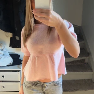 Ljusrosa peplum topp - Säljer en ljusrosa topp med peplum-modell och korta ärmar. Toppen har en rund halsringning och är tillverkad i ett mjukt material. Perfekt för en söt och avslappnad look.