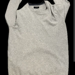 Ljusgrå stickad tröja från bruun & stengade - En stilren ljusgrå stickad tröja från Bruun and stengade. Tröjan har rund halsringning, långa ärmar och ribbade muddar vid ärmslut och nederkant. Perfekt för lager-på-lager under kyliga dagar.