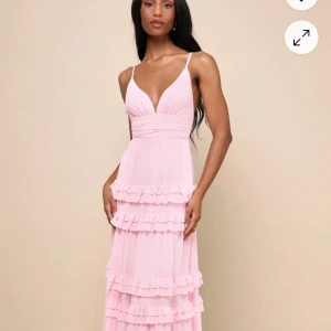 Ljusrosa långklänning med volanger från Lulus  - Säljer min ljusrosa långklänning med smala axelband och djup v-ringning. Klänningen har flera lager volanger längs kjolen och en markerad midja. Perfekt till balen säljer då jag köpte två med olika storlekar❤️ helt slutsåld på Lulus hemsida  