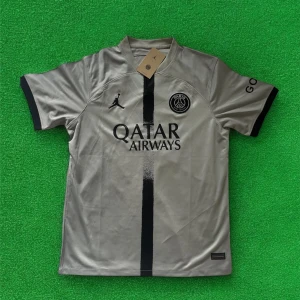 PSG fotbollströja i silvergrått - Säljer en PSG fotbollströja i silvergrått med svart vertikal rand och svarta detaljer. Tröjan har korta ärmar, Qatar Airways som sponsor och PSG-logga på bröstet. Tillverkad i ett lätt och sportigt material.