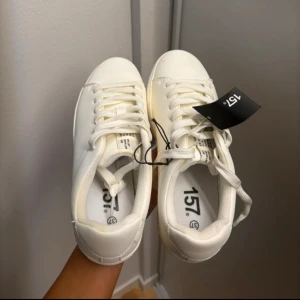 Vita sneakers från 157 - Säljer ett par klassiska vita sneakers från 157 i storlek 37, passar 38. Skorna har en stilren design med snörning och platt sula, perfekta till många olika outfits. Materialet är syntet och de har rund tå. Passar perfekt nu till sommaren😍🍓