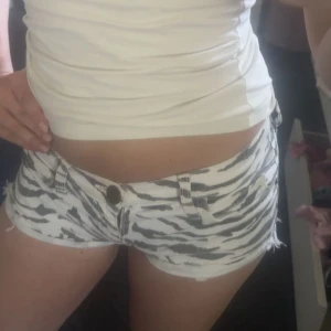 Zebramönstrade jeansshorts - Säljer ett par vita jeansshorts med svart zebramönster. Shortsen är superkorta med råa kanter och har klassiska fickor och bälteshällor. Perfekta för sommaren när du vill sticka ut lite extra.