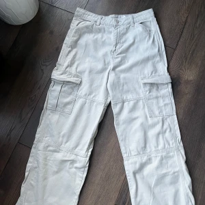 Beige cargobyxor med fickor - Säljer ett par vita cargopants med varsin stora ficka på sidorna. Byxorna har en rak passform och är tillverkade i ett mjukt bomullsmaterial. Helt oanvända