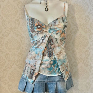 Mönstrad linnetopp med knytning - Säljer en unik mönstrad linnetopp i blå och orange toner. Toppen har smala axelband och en dekorativ knutdetalj framtill. Perfekt för sommardagar och ger en bohemisk känsla.