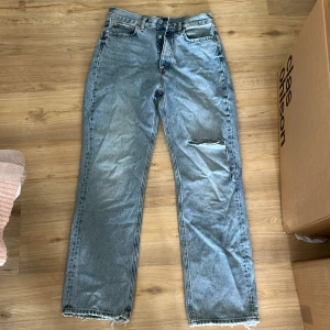Blå raka jeans från Zara med slitning - Säljer ett par ljusblå raka jeans från Zara i storlek 38. Jeansen har en stor sliten detalj på ena benet och råa, fransiga benslut för en cool, avslappnad vibe. Klassisk femficksmodell och tillverkade i bomull. Säljer då de tyvärr är för stora för mig, långa i benen, de passar på mig som är 170 cm.