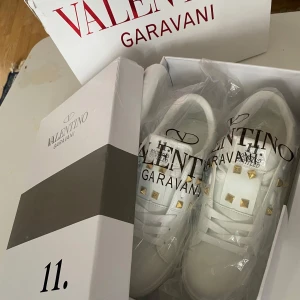 Valentino Rockstud vita sneakers - Snygga vita Valentino Rockstud sneakers med guldiga nitar och klassisk logga på plösen. Skorna är i skinn med vita snören och har en stilren, chunky sula. Perfekta för dig som vill sticka ut med exklusiva detaljer och lyxig känsla. Pris går att diskuteras,alltid aktiv☺️