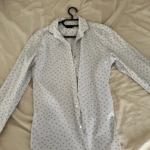 Vit mönstrad skjorta från Zara Man - Vit skjorta från Zara Man i slim fit med små blå mönster och diskreta prickar över hela tyget. Klassisk krage, långa ärmar och knäppning framtill. Perfekt för dig som gillar stilrena men ändå unika detaljer. Den passar runt omkring S och M 