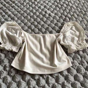 Vit blus med puffärmar från SHEIN - Supersöt vit blus från SHEIN med bred, axelbandslös halsringning och stora puffärmar i broderad spets. Toppen har en croppad passform och är perfekt för dig som gillar romantiska detaljer och volym på ärmarna.