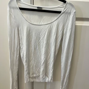 Vit långärmad topp från Gina Tricot - En basic vit långärmad topp från Gina Tricot i mjuk bomull. Modellen har en djup rundad urringning och sitter figurnära. Perfekt att styla med jeans eller kjol för en clean och enkel look.
