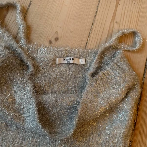 Glittrig silver linnetopp från NA-KD - Supersnygg glittrig silverfärgad linnetopp från NA-KD. Toppen är croppad med smala axelband och har en fluffig, stickad känsla med massor av lyster. Perfekt för dig som vill sticka ut och addera lite extra bling till din outfit!