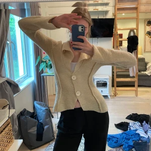 Beige cardigan jacka med stora knappar - Säljer en beige cardigan jacka med två stora vita knappar framtill och markerad midja. Jackan har lång ärm, bred krage och är i ett mjukt material. 