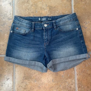 Blå jeansshorts - Snygga blå jeansshorts från You Smile You Mass i klassisk femficksmodell. Shortsen har upprullade benslut, bälteshällor och en normal passform. Perfekta för varma sommardagar och enkla att matcha med allt.
