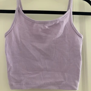 Ljuslila ribbad linnetopp - Superfin ljuslila linnetopp med smala axelband och ribbad struktur. Croppad modell som passar perfekt till höga jeans eller kjol. Mjuk och stretchig, perfekt för varma dagar eller lager på lager.