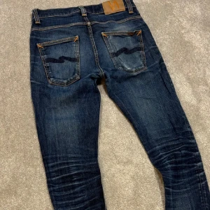 Nudie jeans  - Säljer ett par mörkblå jeans från Nudie Jeans grim trim med klassiska orange sömmar och snygga slitningar på knän och lår. Byxorna sitter slim, dom passar mesta folk som använder W31 L32 men det är storlek W31 L34, passar någon mellan 170-185. Passar perfekt till svart skjorta eller svart hoodie. Perfekt till sommaren🤩