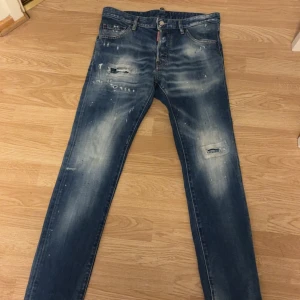 Dsquared2 Cool Guy jeans blå, stl 46 - Snygga Dsquared2 Cool Guy jeans i blå tvätt med slitningar och färgstänk. Klassisk femficksmodell med rakt snitt och coola detaljer som trasiga partier på benen och röd patch bak. Tillverkade i bomull för en skön känsla och stilren look. Pris kan diskuteras vid snabb affär 