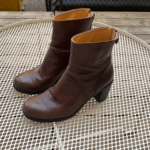 Bruna skinnboots från HOPE, storlek 38 - Snygga bruna boots från HOPE i äkta skinn, tillverkade i Italien. Modellen har rund tå, låg klack och dragkedja bak. Perfekta till höst- och vinterlooken, med klassisk och stilren design som funkar till det mesta. Dragkedja och spenna funkar perfekt och skorna är i bra skick. Pris kan diskuteras!