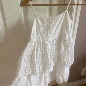 Vit volangklänning från Gina Tricot - Superfin vit klänning från Gina Tricot med tunna axelband och volanger. Klänningen har små guldiga detaljer i tyget. Perfekt för varma dagar. Skriv till mig privat om ni vill köpa💗💗
