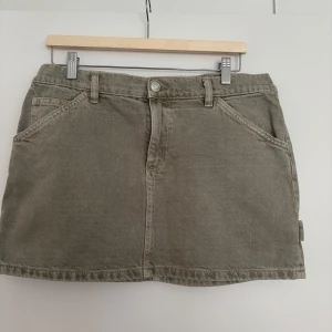 Militärgrön jeanskjol från MNG - Snygg militärgrön jeanskjol från MNG med klassisk femficksdesign, bälteshällor och dragkedja framtill. Kjolen är kort och har raka linjer, perfekt till sneakers eller boots. Materialet är slitstarkt och ger en cool vardagslook.