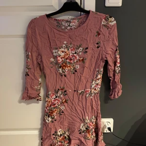 Blommig rosa klänning från NLY Trend - Supersöt rosa kortklänning från NLY Trend med blommigt mönster och trekvartsärm. Klänningen har öppen rygg och volangdetaljer vid ärmslut. Perfekt för dig som gillar romantisk och feminin stil.