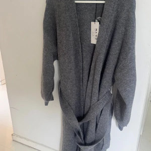 Grå lång kofta från NA-KD med bälte - Mysig lång grå kofta från NA-KD med bälte i midjan och långa ärmar. Koftan är stickad och har en avslappnad passform, perfekt att slänga på sig över en t-shirt eller topp. Enkel och stilren design som funkar året runt.