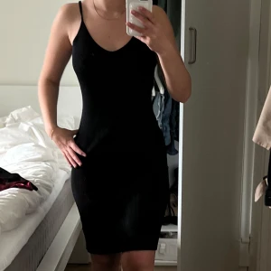 Svart ribbad klänning - Säljer en svart ribbad klänning med smala axelband  och v-ringning. Klänningen är perfekt för dig som gillar en enkel men snygg look. Materialet är jätte stretchigt, vilket gör klänningen superbekväm att bära.