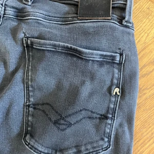 Replay Anbass svarta jeans, stl 29 - Snygga svarta Replay Anbass jeans i slim fit med klassisk femficksdesign och diskret logga på bakfickan. Jeansen har en mörk tvätt och raka ben, tillverkade i stretchig bomullsdenim för skön passform. Längd 30.