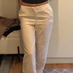 Beiga vida linnebyxor med snörning - Snygga ljus beiga linnebyxor med avslappnad passform och vida ben. Byxorna har låg midja och justerbar snörning i midjan för extra komfort. Perfekta för en chill och stilren look under varmare dagar. Väldigt sällan använda. 