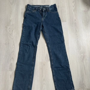 Mörkblå straight jeans midwaist - Snygga mörkblå jeans med rak passform och klassisk femficksdesign. Midjan är midwaist och byxorna har en enkel knappstängning framtill. Perfekta för dig som gillar en tidlös och clean look.