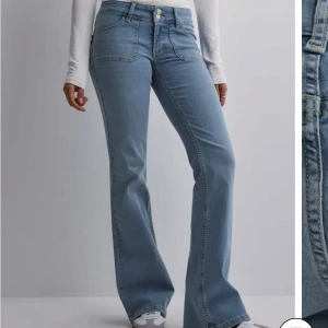 Ljusblå bootcut jeans  - Snygga ljusblå bootcut jeans med låg midja och stora framfickor. Jeansen har två bakfickor med lock och silverknappar. Tillverkade i klassiskt denimtyg. Innerbenslängden är 83cm, men man skulle även kunna sprätta upp nederkanten för att få den längre!! Så himla snygga jeans som funkar med allt!!!