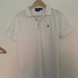 Vit pikétröja Polo Ralph Lauren M - Golf piké. Klassisk vit pikétröja från Polo Ralph Lauren i custom slim fit. Tröjan har korta ärmar, krage och knäppning med tre knappar. Ikoniska blå loggan broderad på bröstet. Perfekt för en clean och stilren look.