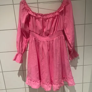 Rosa offshoulder klänning Amisu - Supersöt rosa kortklänning från Amisu inköpt på Newyorker med offshoulder-modell, långa ärmar och volangdetaljer vid ärmslut och fåll. Smockad midja ger en snygg passform. Endast använd en gång. 