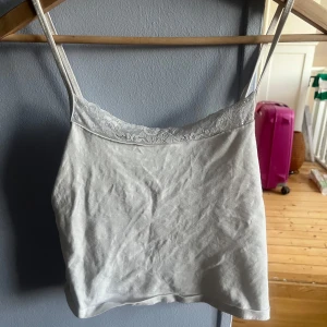 Vit croppad linnetopp med spets - Supersöt vit croppad linnetopp från Gina Tricot med tunna axelband och spetsdetalj längs halsringningen. Säljer då jag knappt använder den! Sitter fint på och är lite längre än vad den ser ut!