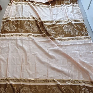 Gardin - Säljer en stor vanlig gardin i beige och brunt med vackert blommönster. Gardinens kanter har en fin fransdetalj som ger en extra touch av stil. Längd: 248 cm och Bredd: 141cm. (Det är en gardin men vet inte vilken slags men den är inte så tunn)