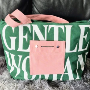 Grön snygg Gentle Woman väska - Jättefin grön väska i canvas med snyggt randigt bomulls innerfoder från Gentle Woman Väskan har 2st rosa handtag och den stängs med en dragkedja  Den har ett stort rymligt innerfack + ett litet innerfack med dragkedja  H32cm/B46cm/D16cm Väskan är ny i jättefint skick!