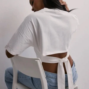 Vit croppad topp med knyt i ryggen - Säljer en vit croppad topp med korta ärmar och snygg knytning i ryggen. Toppen har öppen rygg och är perfekt att styla med jeans eller kjol. 