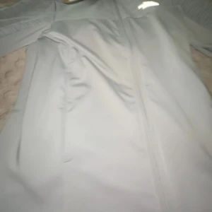 Ljusgrå vindjacka från The North Face - Snygg ljusgrå vindjacka från The North Face med hel dragkedja framtill och reflekterande detaljer. Jackan har långärmade ärmar och är tillverkad i lätt polyester som passar perfekt för utomhusaktiviteter. Stilren design med diskret logga på bröstet.