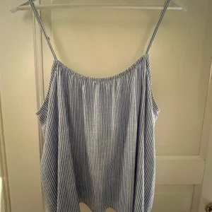 Randig blå linnetopp från H&M - Säljer en chill blåvit randig linnetopp från H&M i storlek M. Toppen har tunna justerbara axelband och en lös passform som ger en skön vibe. Materialet är 80% bomull och 20% linne, perfekt för varma dagar. Knappdetalj bak. Fråga om du vill ha fler bilder!