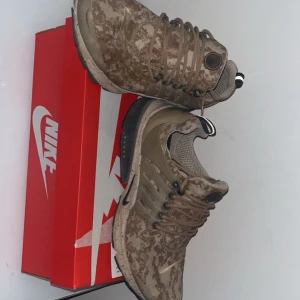 Nike Presto camo sneakers beige. Nike skor som är knappast använda  - Nike Presto sneakers i beige och bruna toner med digitalt camouflage-mönster. Skorna har snörning, rund tå och platt sula. Ovandelen är i syntet och mesh för skön komfort. Snygga detaljer med prickig mellansula och svart Nike-logga på sidan.