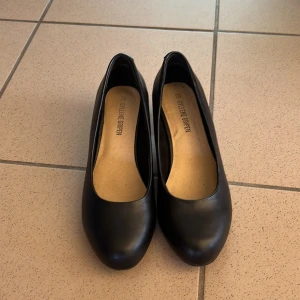 Svarta pumps från Gyllene Gripen - Stilrena svarta pumps från Gyllene Gripen med rund tå och låg klack. Skorna är tillverkade i skinn och har en klassisk, enkel design som passar till många olika outfits. Perfekt för dig som gillar tidlös stil och vill ha ett par bekväma klackar.