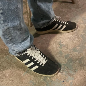 Adidas Gazelle svart  - Säljer ett par schyssta svarta Gazelle. Dessa har mycket kvar att ge trots att mockan bleknat något och att sulan vid hälen är lite småskadad. Passar 44-45. Hör av dig vid frågor eller för prisdiskussion!