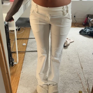 Vita bootcut kostymbyxor med fickor - Snygga vita bootcut kostymbyxor med låg midja och stilrena fickdetaljer både fram och bak. Byxorna har två knappar i midjan och är tillverkade i ett mjukt bomullsmaterial som sitter skönt. Perfekta för dig som gillar en clean och fräsch look. ENDANST PROVADE!