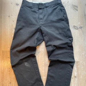Svarta Dickies 874 Original byxor - Svarta Dickies 874 Original byxor med klassisk rak passform och breda hällor. Byxorna har två sidofickor och två bakfickor, varav en med Dickies-logga. De har en liten defekt på knät (se bild) men inget jag tycker man tänker på. Skriv vid intresse!