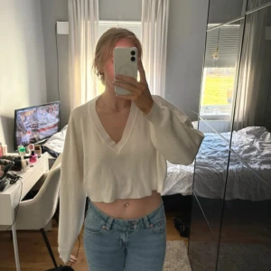 Vit croppad v-ringad tröja - Säljer en vit croppad tröja med v-ringad hals och långa ärmar. Tröjan har en loose passform och är perfekt för dig som gillar en chill och trendig stil. Materialet känns mjukt och lätt, vilket gör den skön att bära. Passar till jeans eller kjol för en snygg look.