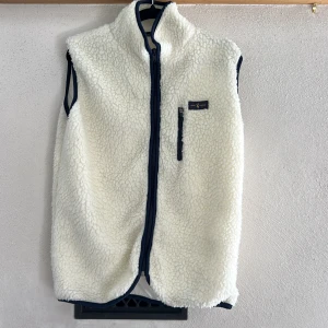 Vit fleeceväst från North Couture XS - Mysig vit fleeceväst från North Couture i storlek XS. Västen har en hög krage, mörkblå detaljer och dragkedja framtill samt en praktisk bröstficka med dragkedja. Perfekt för lager-på-lager och chill dagar. Använd max 5 ggr.😁